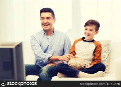 family, people, technology, television and entertainment concept - happy father and son with popcorn watching tv at home. smiling father and son watching tv at home