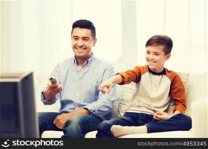 family, people, technology, television and entertainment concept - happy father and son with remote control watching tv at home. smiling father and son watching tv at home