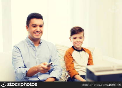 family, people, technology, television and entertainment concept - happy father and son with remote control watching tv at home. smiling father and son watching tv at home