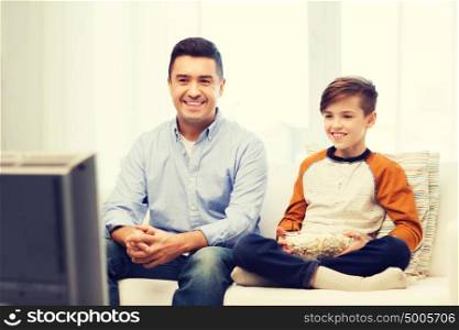 family, people, technology, television and entertainment concept - happy father and son with popcorn watching tv at home. smiling father and son watching tv at home
