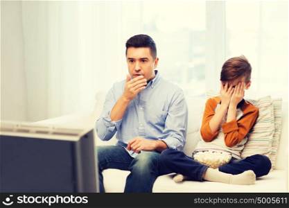 family, people, technology, television and entertainment concept - scared father and son watching horror movie on tv at home. father and son watching horror movie on tv at home
