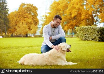 family, pet, animal and people concept - happy man with labrador retriever dog walking in autumn city park