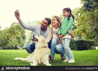 family, pet, animal, technology and people concept - happy family with labrador retriever dog taking selfie by smartphone in park. happy family with dog taking selfie by smartphone