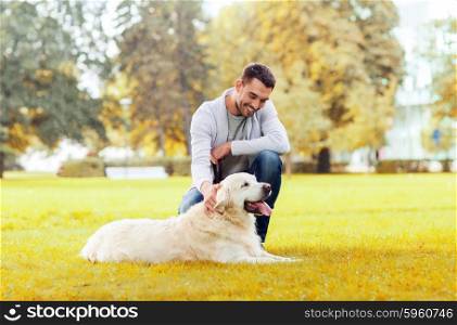 family, pet, domestic animal, season and people concept - happy man with labrador retriever dog walking autumn in city park