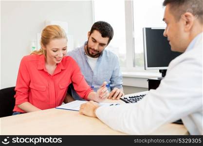 family planning, medicine, fertility and healthcare concept - couple visiting doctor and filling form at clinic. couple visiting doctor at family planning clinic