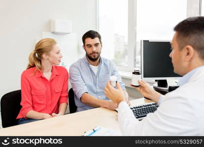 family planning, medicine, fertility and healthcare concept - doctor showing medications to young couple at clinic. doctor showing medicine to family couple at clinic