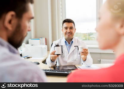 family planning, medicine, fertility and healthcare concept - doctor showing medications to young couple at clinic. doctor showing medicine to family couple at clinic