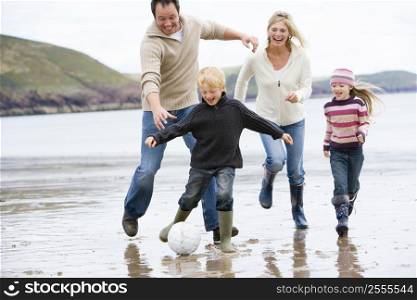 Family playing soccer at beach smiling