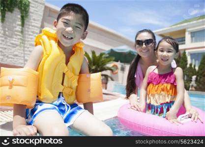 Family portrait, mother, daughter, and son, by the pool with pool toys