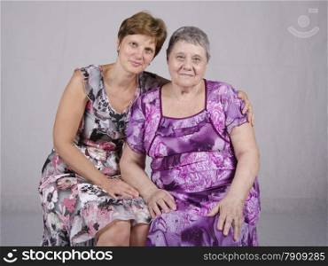 Family portrait of two women: the mother (80 years old) and a daughter (50 years). Studio light background