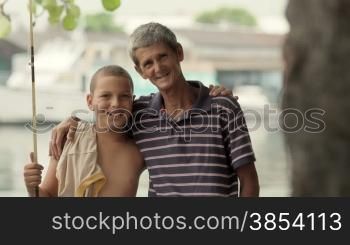 Family portrait with happy boy and grandfather hugging and smiling at camera after fishing near river