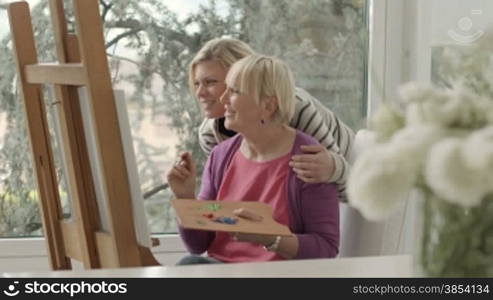 Family portrait with happy mother painting for hobby and daughter smiling and hugging her at home. Dolly shot