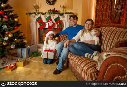 Family posing at living room decorated for Christmas with burning fireplace