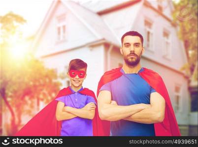 family, power and people concept - man and boy wearing mask and red superhero cape over house background. man and boy wearing mask and red superhero cape