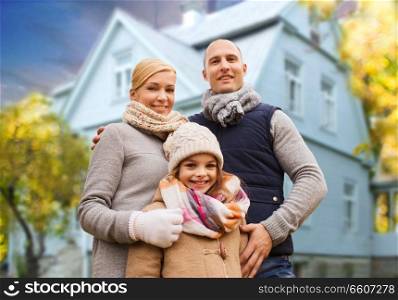 family, real estate and people concept - happy mother, father and daughter over living house background outdoors in autumn. happy family over living house in autumn
