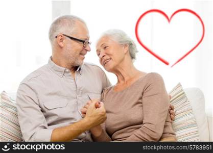 family, relations, love, age and people concept - happy senior couple hugging and holding hands on sofa at home with big red heart shape