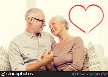 family, relations, love, age and people concept - happy senior couple hugging and holding hands on sofa at home with big red heart shape