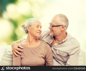 family, relations, love, age and people concept - happy senior couple hugging and looking at each other on sofa over green background