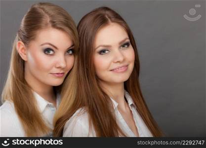 Family relationships, friendship concept. Happy two beautiful women sisters, blonde and brunette having fun. Studio shot on grey background. Two beautiful women, blonde and brunette having fun