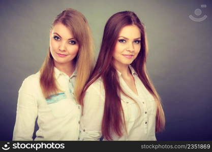 Family relationships, friendship concept. Happy two beautiful women sisters, blonde and brunette having fun. Studio shot on grey background. Two beautiful women, blonde and brunette having fun