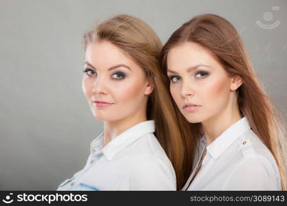 Family relationships, friendship concept. Happy two beautiful women sisters, blonde and brunette having fun. Studio shot on grey background. Two beautiful women, blonde and brunette having fun