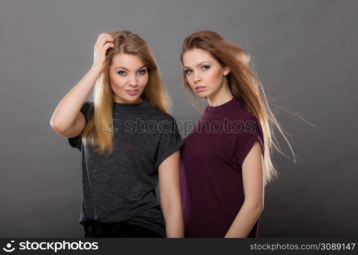 Family relationships, friendship concept. Two beautiful women sisters, blonde and brunette with windblown hair posing charmingly. Studio shot on dark grey background. Two beautiful women, blonde and brunette posing