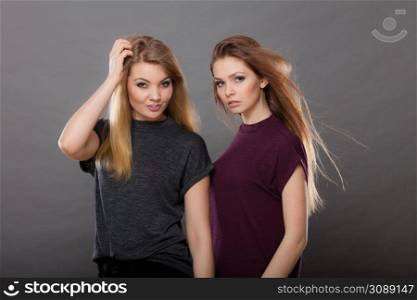 Family relationships, friendship concept. Two beautiful women sisters, blonde and brunette with windblown hair posing charmingly. Studio shot on dark grey background. Two beautiful women, blonde and brunette posing
