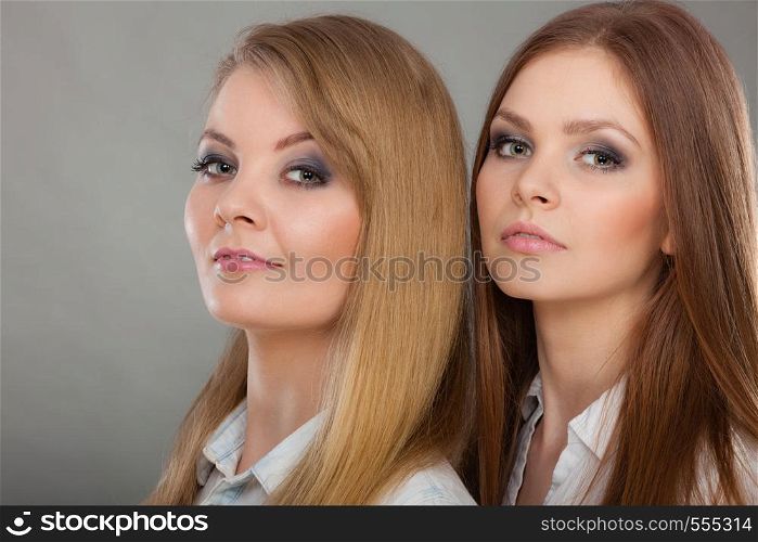 Family relationships, friendship concept. Two beautiful women sisters, blonde and brunette with windblown hair posing charmingly.. Two beautiful women, blonde and brunette posing