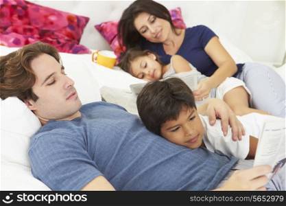 Family Relaxing In Bed With Coffee And Newspaper