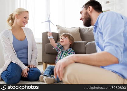 family, renewable energy, ecology and people concept - happy little boy and parents playing with toy wind turbine at home. happy family playing with toy wind turbine