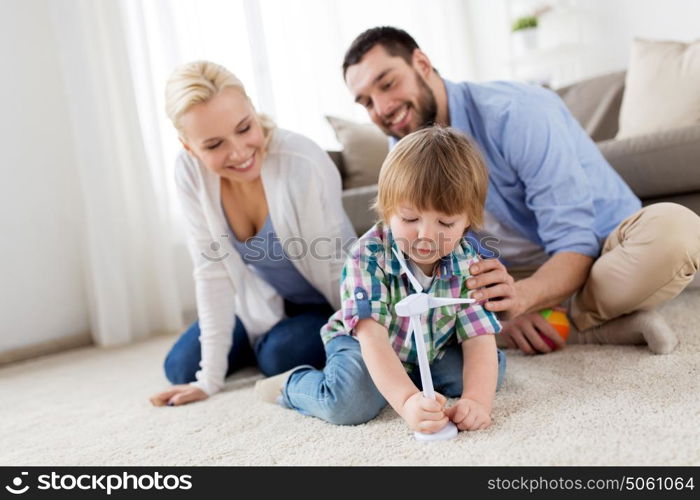 family, renewable energy, ecology and people concept - happy little boy and parents playing with toy wind turbine at home. happy family playing with toy wind turbine