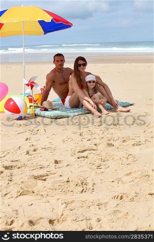 Family sat on the beach by parasol