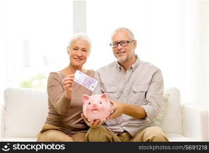 family, savings, age and people concept - smiling senior couple with money and piggy bank at home