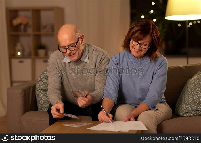 family, savings and people concept - smiling senior couple with bills counting money at home. senior couple with bills counting money at home