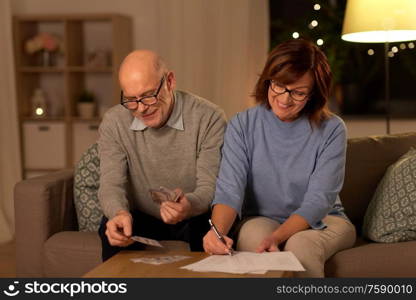 family, savings and people concept - smiling senior couple with bills counting money at home. senior couple with bills counting money at home