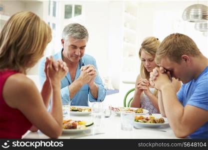 Family Saying Prayer Before Eating Meal At Home Together