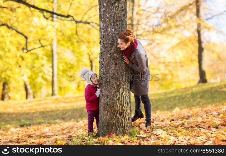 family, season and people concept - happy mother and little daughter at tree trunk playing in autumn park. happy mother and little daughter at autumn park. happy mother and little daughter at autumn park