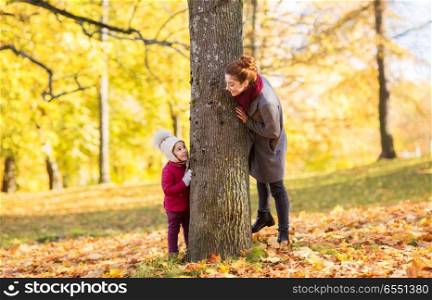 family, season and people concept - happy mother and little daughter at tree trunk playing in autumn park. happy mother and little daughter at autumn park. happy mother and little daughter at autumn park