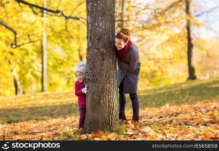 family, season and people concept - happy mother and little daughter at tree trunk playing in autumn park. happy mother and little daughter at autumn park