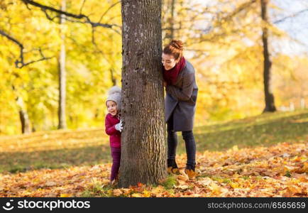 family, season and people concept - happy mother and little daughter at tree trunk playing in autumn park. happy mother and little daughter at autumn park