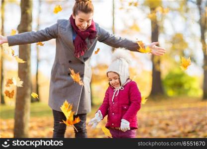 family, season and people concept - happy mother and little daughter playing with autumn leaves at park. happy family playing with autumn leaves at park. happy family playing with autumn leaves at park
