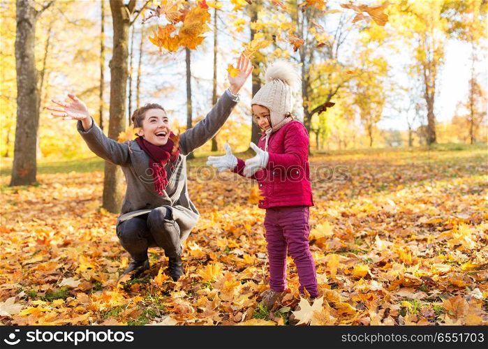 family, season and people concept - happy mother and little daughter playing with autumn leaves at park. happy family playing with autumn leaves at park. happy family playing with autumn leaves at park