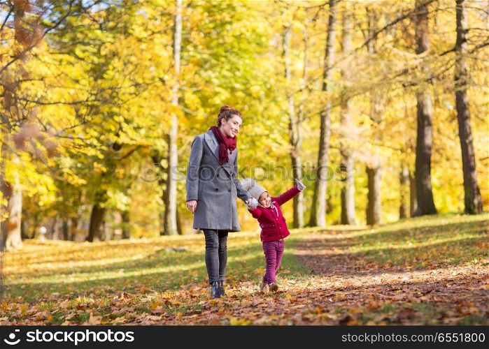 family, season and people concept - happy mother and little daughter walking along autumn park. happy mother and little daughter at autumn park. happy mother and little daughter at autumn park