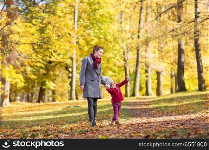 family, season and people concept - happy mother and little daughter walking along autumn park. happy mother and little daughter at autumn park. happy mother and little daughter at autumn park