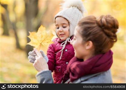 family, season and people concept - happy mother and little daughter with maple leaf at autumn park. happy mother with little daughter at autumn park