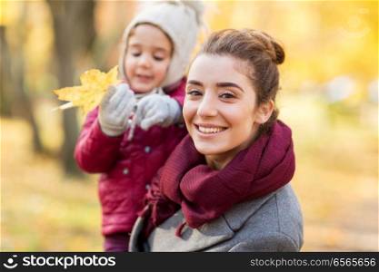family, season and people concept - happy mother and little daughter with maple leaf at autumn park. happy mother with little daughter at autumn park