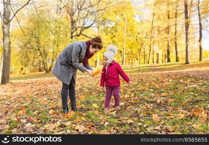 family, season and people concept - happy mother and little daughter with autumn leaves at park. happy family with autumn leaves at park