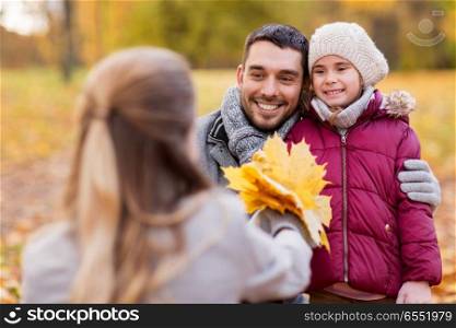 family, season and people concept - happy mother, father and little daughter with maple leaves at autumn park. happy family with maple leaves at autumn park. happy family with maple leaves at autumn park