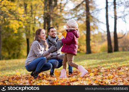 family, season and people concept - happy mother, father and little daughter with maple leaves at autumn park. happy family with maple leaves at autumn park