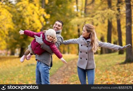family, season and people concept - happy mother, father and little daughter playing at autumn park. happy family playing at autumn park. happy family playing at autumn park